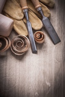 Wooden mallet curled up shavings flat chisels leather gloves on wood board vertical view