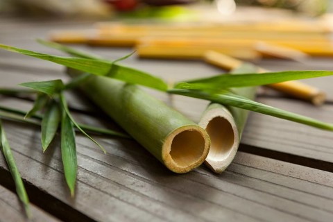 Round bamboo sticks with leaves on wooden background. Ecological raw material