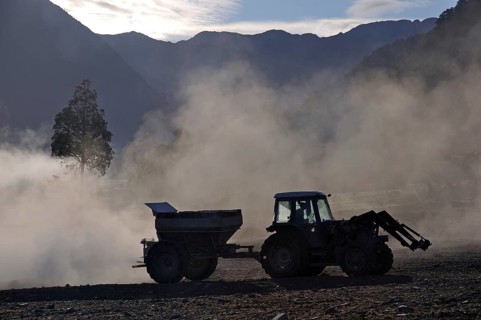 Tractor spreading lime with a fertiliser spreader, West Coast, New Zealand