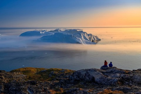 Large glaciers in the bay by the rocky shore in the light of the setting sun with fog over the