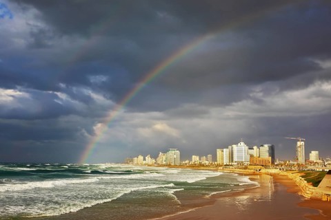 Storm cloud hanging over the sea, gorgeous huge rainbow crossed the sky. Promenade and beach in Tel