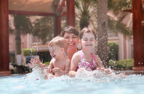 Overjoyed mother with little daughter and son laughing while playing together in swimming pool with