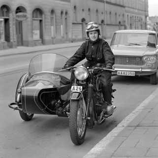 In the 1960s. A woman seen dressed in the typical motorcycle drivers outfit and helmet at her
