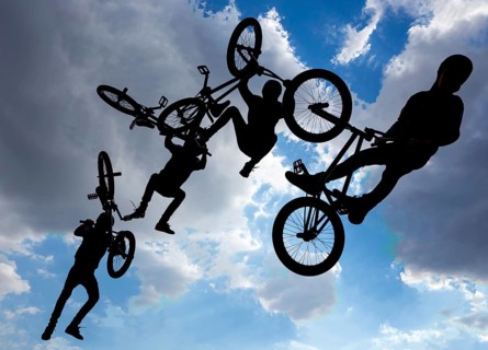 An extreme rider is making a free style jump from a ramp. The young boy with his bicycle is seen as