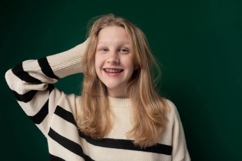 A woman with blonde hair is standing, wearing a striped sweater. She appears calm and is looking