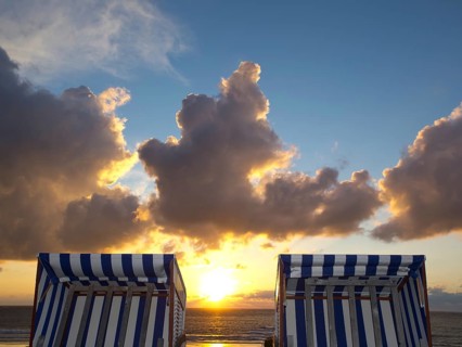 Two empty beach chairs enjoy the view of a golden sunset, norderney, north sea, germany