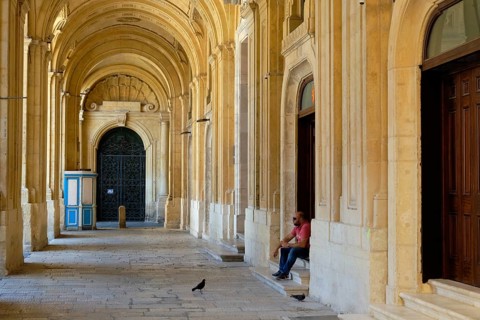 A man with his sandwich and two hungry pigeons in the archway of the National Library, Valletta,