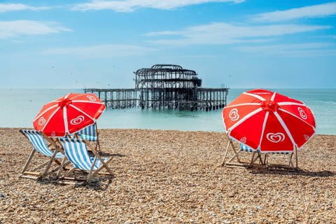 Folding chairs with parasols on the beach in front of the ruins of the burnt down West Pier in