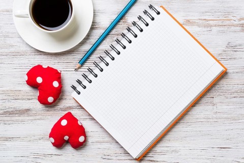 Coffee cup notepad pencil and two red hearts on wooden surface