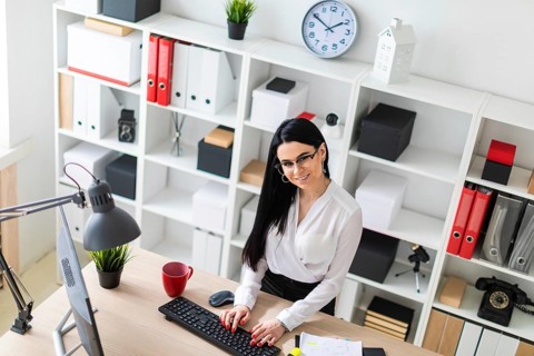 A young girl with glasses, wearing a white blouse and black trousers, works in the office. The girl