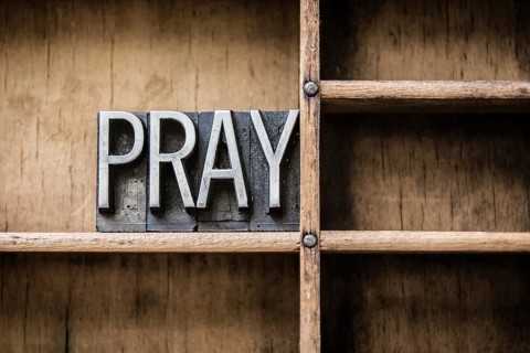The word PRAY written in vintage letterpress type sitting in a wooden drawer