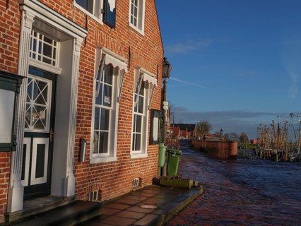 A sunny harbour street with brick houses and water in the background, Greetsiel, East Frisia,