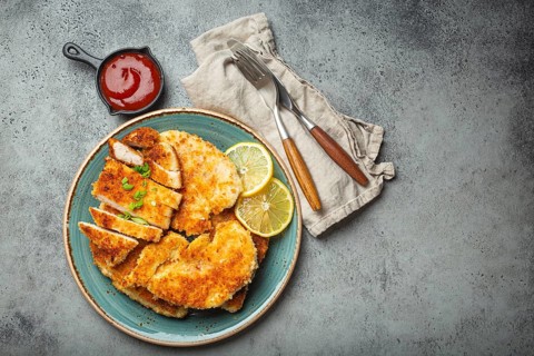 Crispy panko breaded fried chicken fillet with green salad and lemon cut on plate on gray