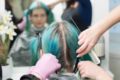 Back view of female head with emerald hair color and regrown hair roots. Woman sits in chair by