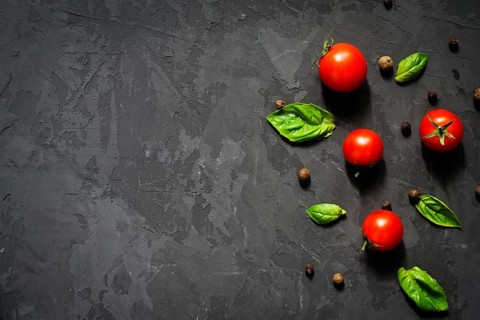 Juicy ripe cherry tomatoes with green basil leaves and black pepper on black background. Health