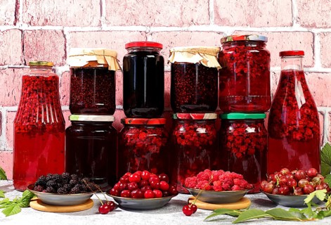 Jars with raspberry, cherry, gooseberry jam and compote on kitchen background with leaves and fresh