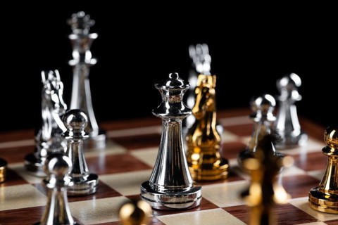 Gold and silver chess figures placed on wooden chessboard. Intellectual duel and tactical battle in