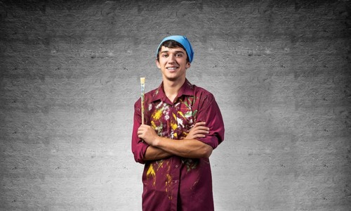 Young happy painter artist holding paintbrush. Portrait of painter in dirty shirt and bandana
