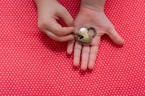 Hand holding a heart shaped lock and key on a red background