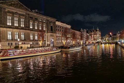 Illuminated boats and buildings are reflected in the canal water at night, Amsterdam, Netherlands