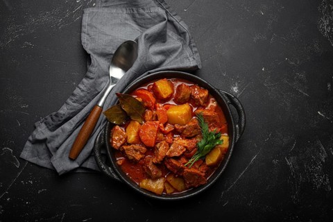 Beef meat stew with potatoes, carrot and delicious gravy in black casserole pot with bay leaves