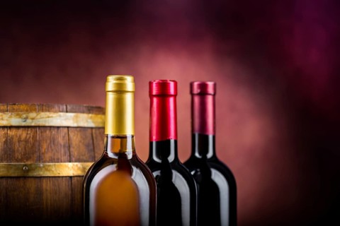 Three bottles of wine and wooden barrel on a burgundy background