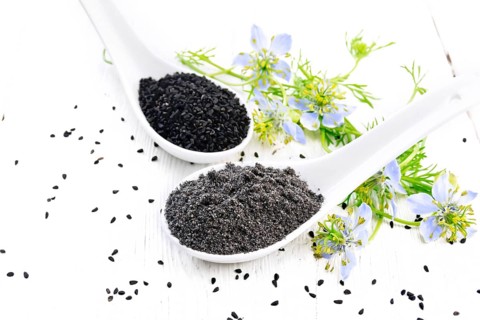 Flour and seeds of Nigella sativa in two spoons, sprigs of kalingini with blue flowers and green