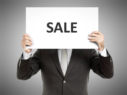 A business man holding a paper in front of his face with the text sale
