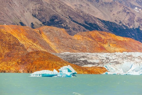 Massive glacier descends into the emerald water. In the water ice-floes, broken away from a glacier