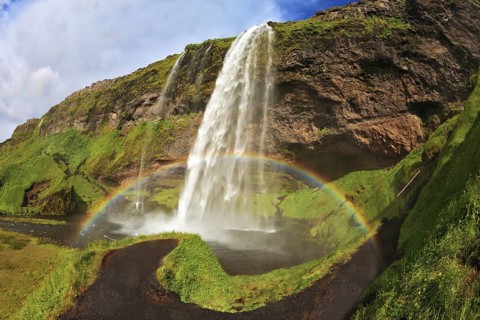 Summer sunny day. Large rainbow decorates a drop of water. Seljalandsfoss waterfall in Iceland. The