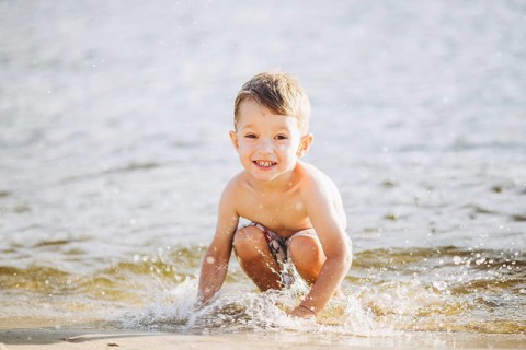 Theme is summer time and rest near the water. Little joyful Caucasian funny boy plays and enjoys in