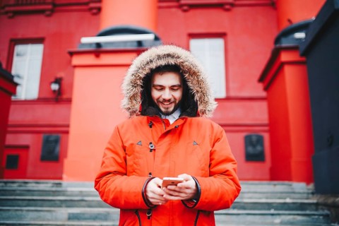Handsome young male student with toothy smile and beard stands on red wall background, facade of