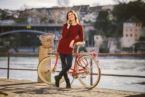 A young female traveler enjoying stands next to a bicycle near a river in the city of Basel.