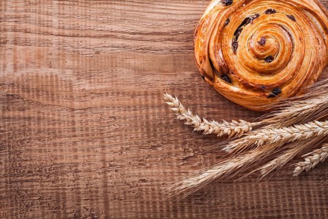 Sweet raisin bun bunch of wheat ears on oak wooden board food and drink concept