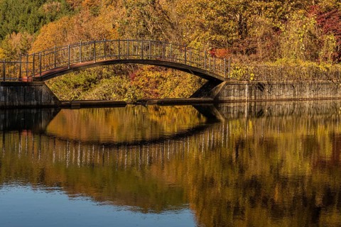 Footbridge over small pond in mountain valley with trees in beautiful fall colors in background,