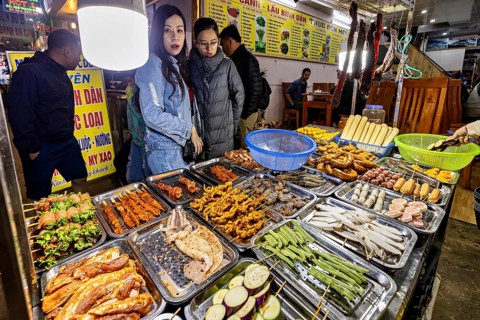 Visitors look at a rich selection of grilled food at a night market, restaurant in the streets of