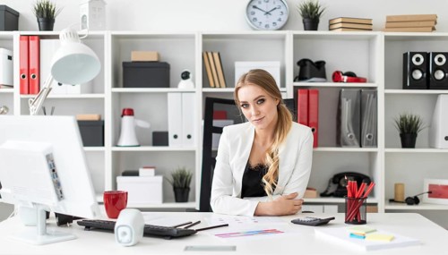 Beautiful young girl with blond hair in a white jacket and black blouse is working in the office.