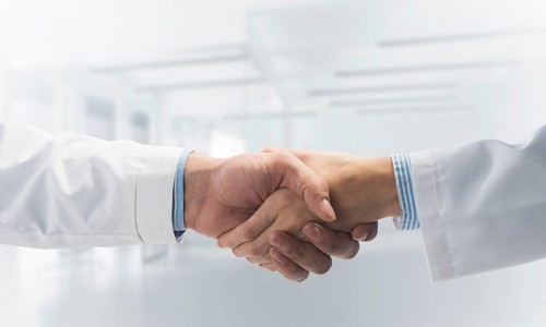 Close-up of the handshake between the two medics. Against the backdrop of the cityscape