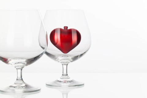 Red heart inside a glass of cognac on a glass plate