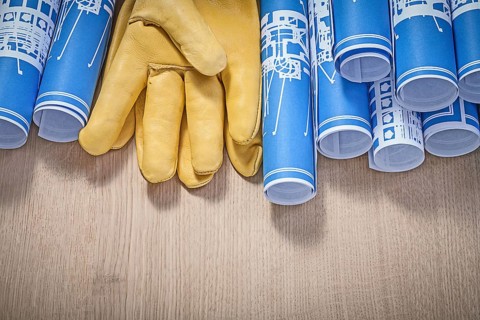 Blue rolled up construction plans leather protective gloves on wood board