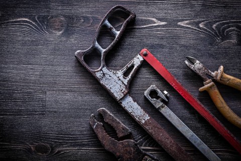 Obsolete vintage handsaw wire-cutter pliers on wooden board construction concept