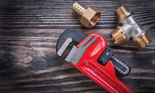 Pipe wrench brass equal tee nipple hose connector on wooden background plumbing concept