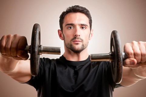 Personal Trainer doing front dumbell raises for training his deltoids in a brown background