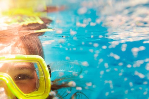 Little girl in colorful swimming mask smiling looking at camera under water