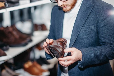 A man inspects a brown leather shoe on a store shelf