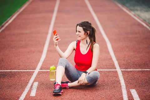 Young woman athlete at the stadium sporting lifestyle, sitting on the track, taking selfie photo on