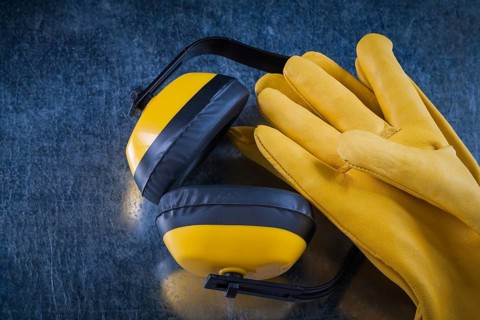 Safety yellow earmuffs and leather construction gloves on scratched metallic surface building