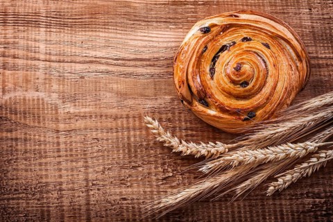 Tasty raisin roll bunch of wheat ears on oak wooden board food and drink concept