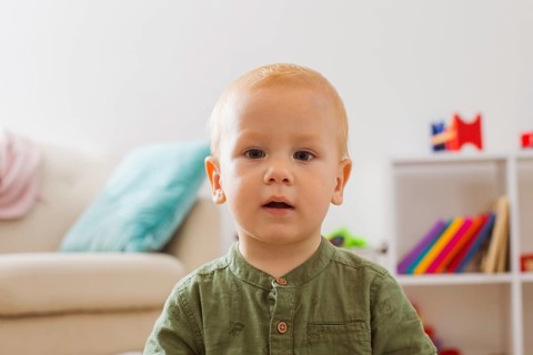 Portrait of a baby boy who is enchanted looks at the camera. The blond boy is sitting in the middle