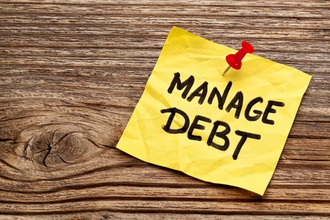 Manage debt - yellow reminder note against grained wood board